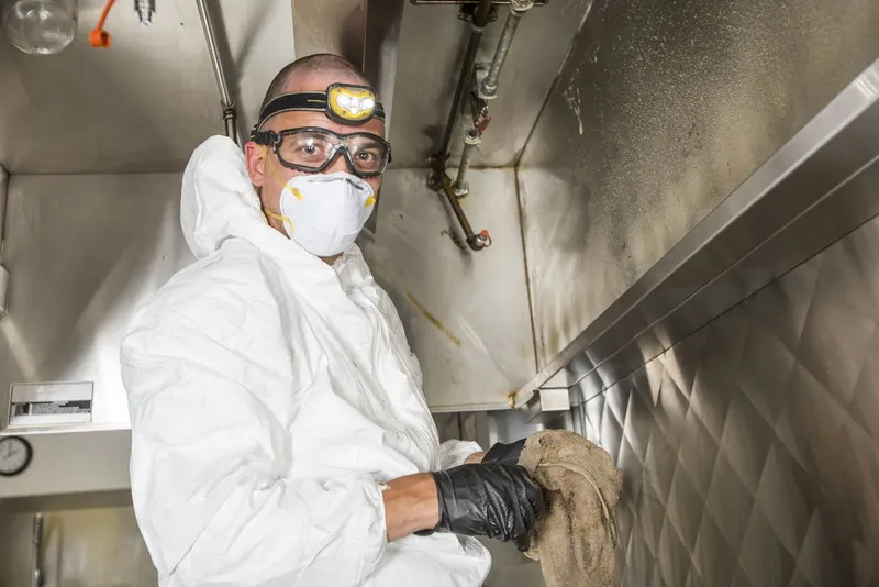 Technician sliding a baffle filter out of the filter slot along the front of a commercial kitchen hood